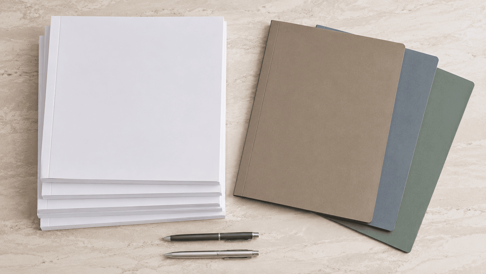 Resmas de papel, esferos y cuadernos sobre una superficie de mármol